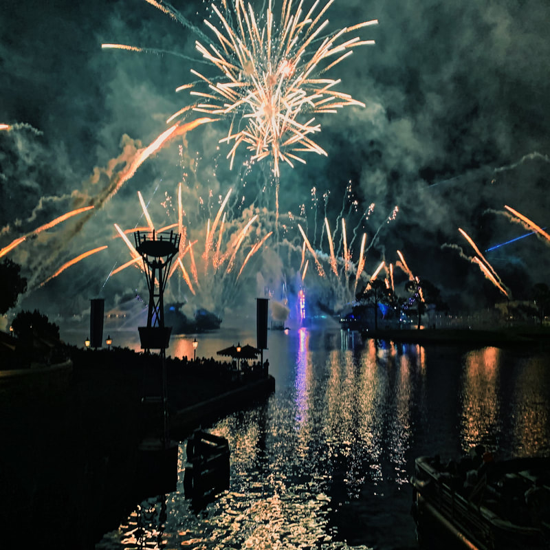 Orange fireworks exploding against a dark sky, reflecting in the water in the foreground