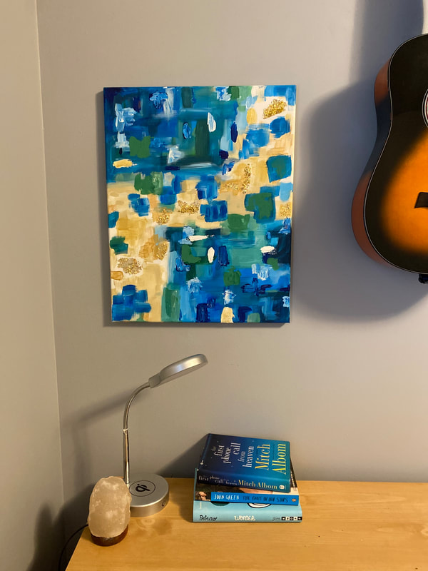 Photograph of abstract painting on a wall; painting is blue, green, yellow, and shimmering gold splotches of color; it hangs next to a guitar over a desk with similarly-colored books